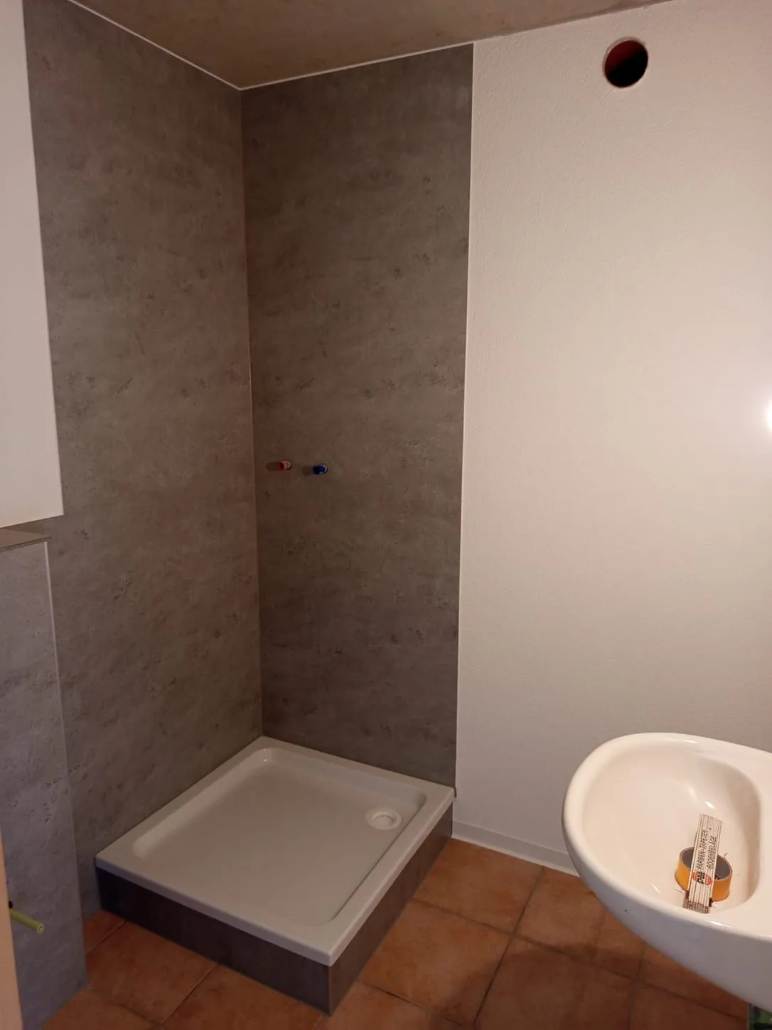Neue Duschecke mit Duschwanne und Wandfliesen in Betonoptik, daneben das Waschbecken