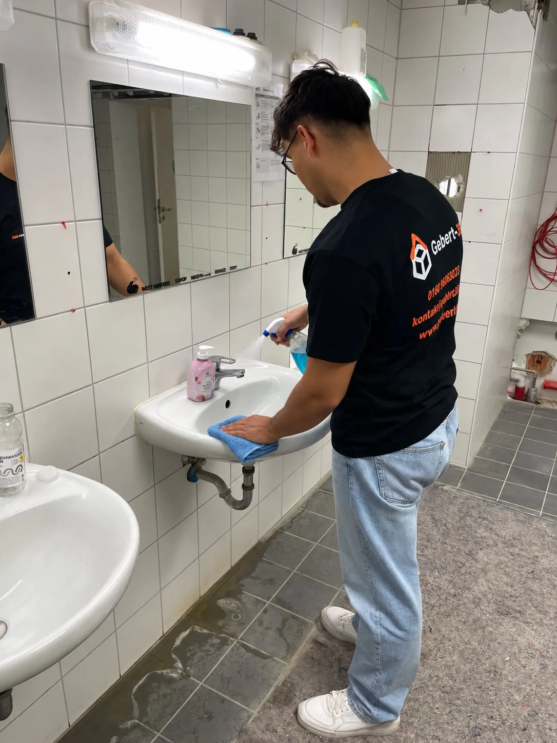 Gebert-360-Mitarbeiter reinigt ein Waschbecken im Sanitärraum mit Tuch und Sprühflasche