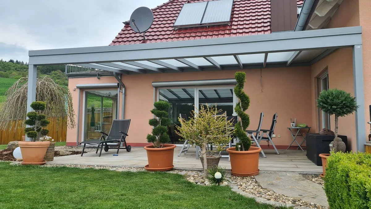 Terrassenüberdachung aus Aluminium mit Glasdach über einer bepflanzten Terrasse an einem Einfamilienhaus