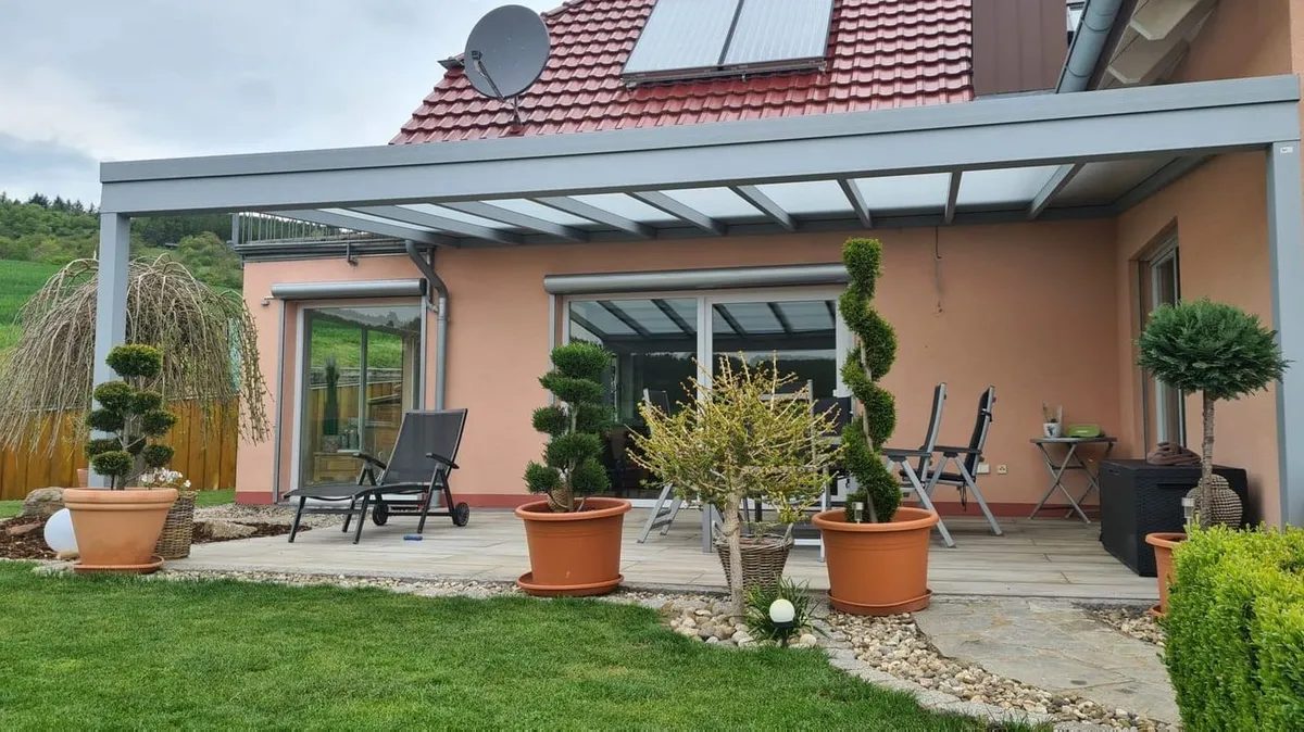 Dieselbe Terrasse nach der Montage: Aluminium-Überdachung mit Glasdach über Kübelpflanzen und Liegen