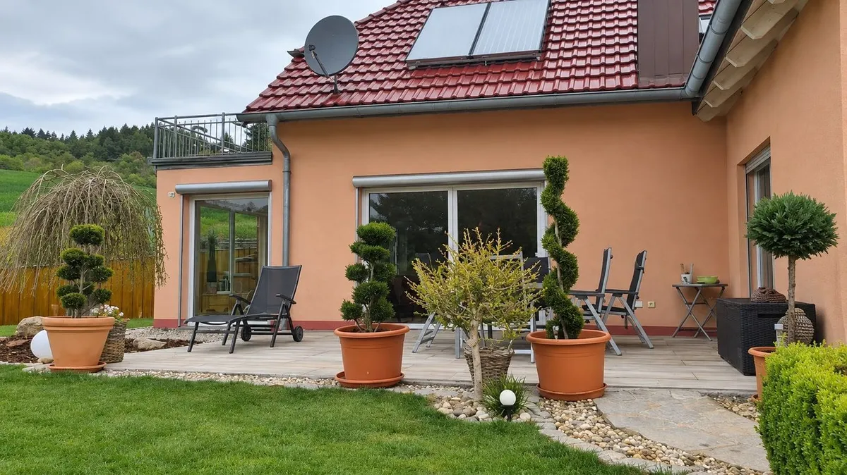 Die Terrasse vor der Montage: Plattenbelag mit Kübelpflanzen und Liegen vor der Hausfassade, noch ohne Überdachung